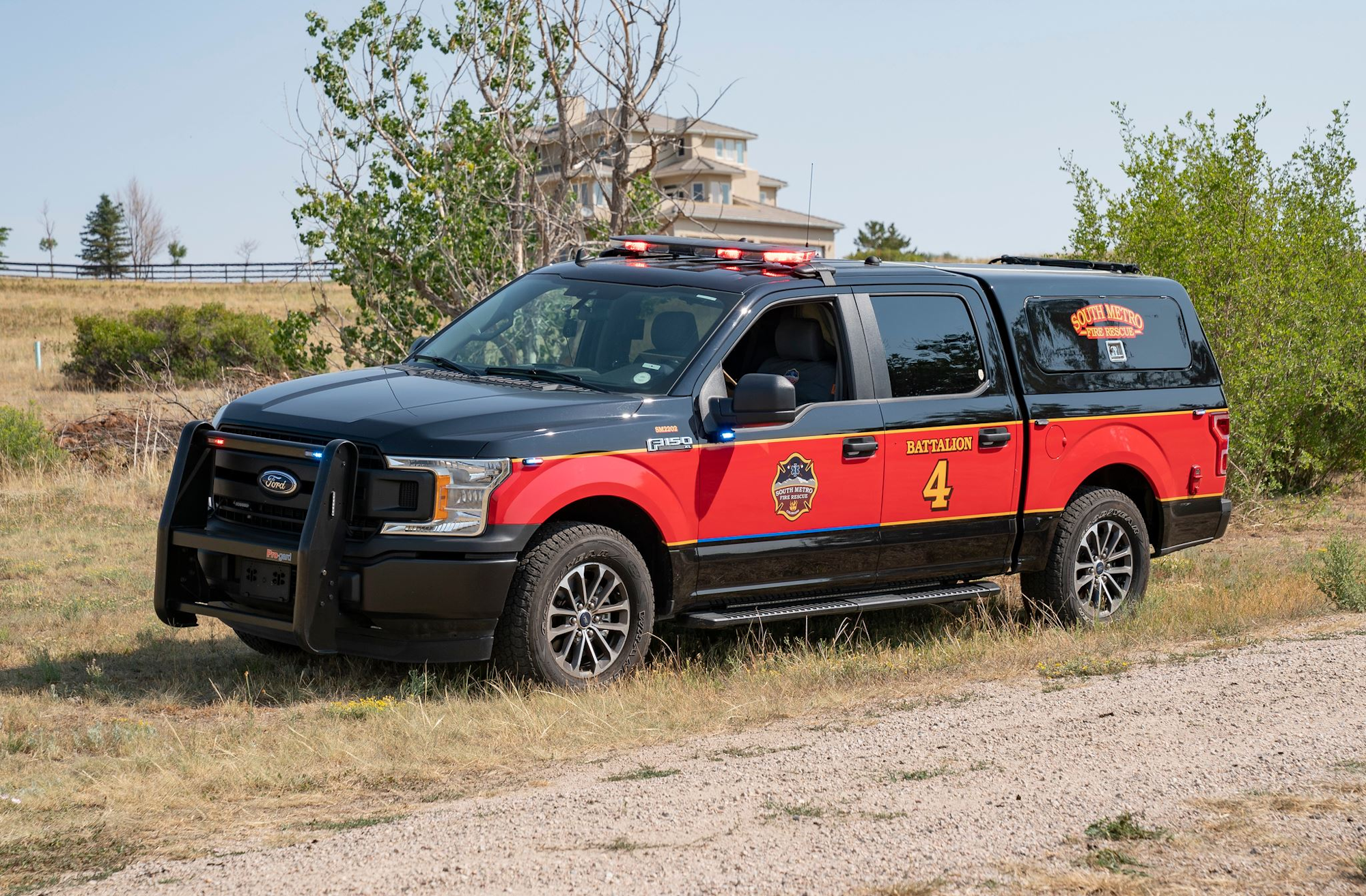Red and black fire rescue vehicle labeled "Battalion 4" parked off-road near some trees.