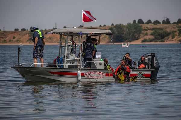 Rescue boat on water with dive rescue team; two divers entering water, red dive flag displayed, calm lake background.