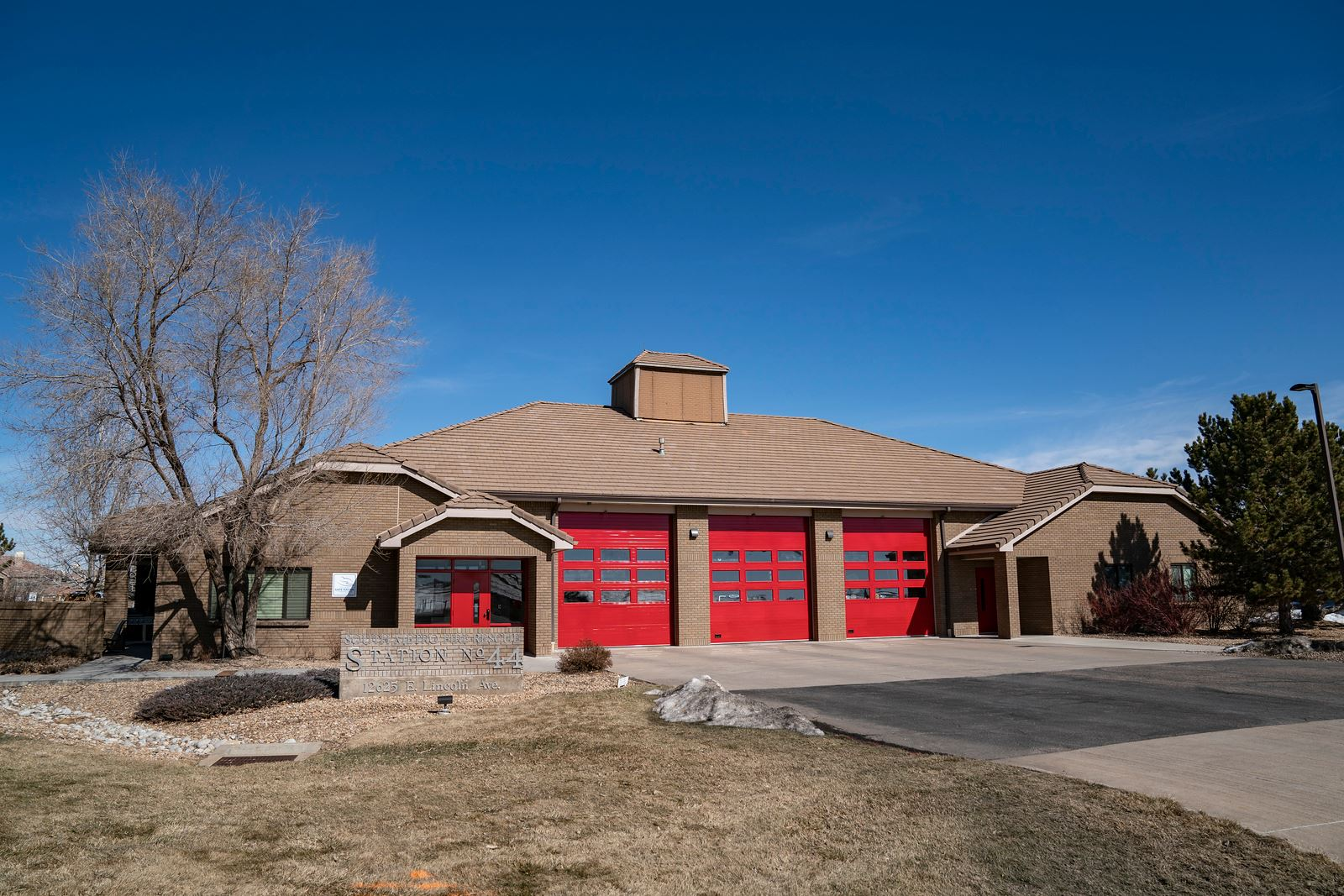 A fire station with red garage doors, a sign reading "Station No. 44" and trees around it under a clear blue sky.