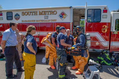 Emergency responders in hazmat gear gather near a South Metro Hazardous Materials Unit truck.