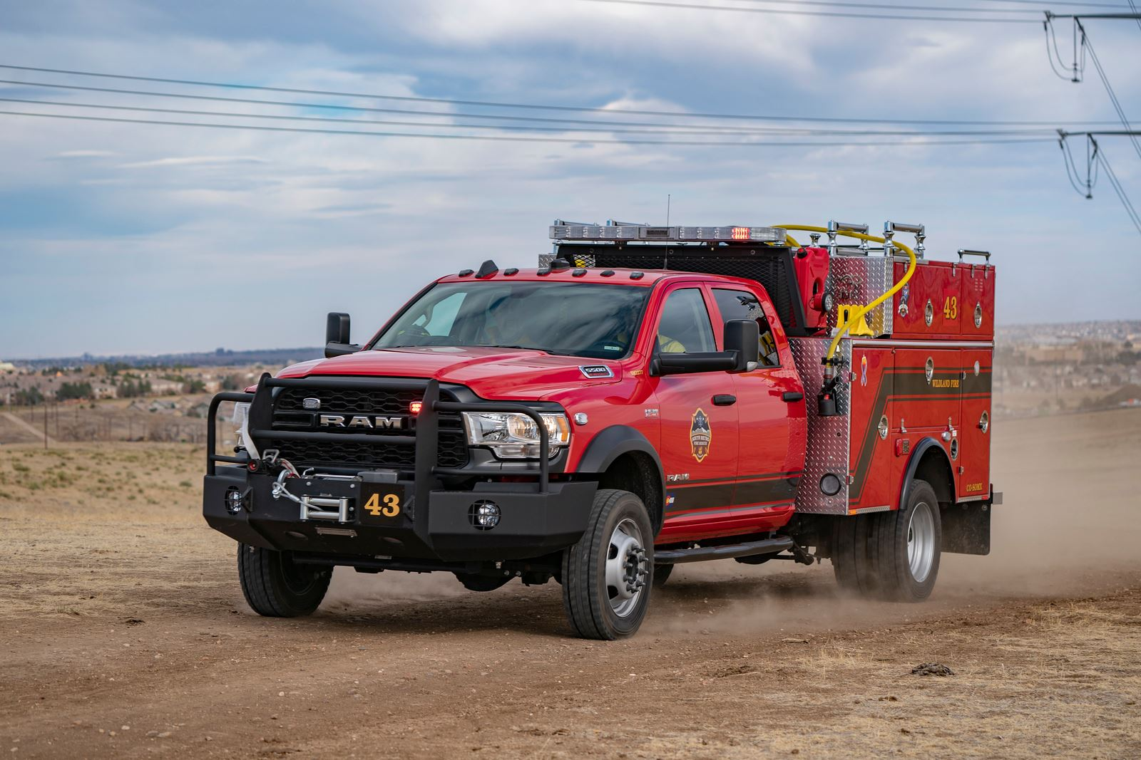 Red fire truck driving on a dirt road, marked with number 43, equipped with emergency lights and fire-fighting equipment.