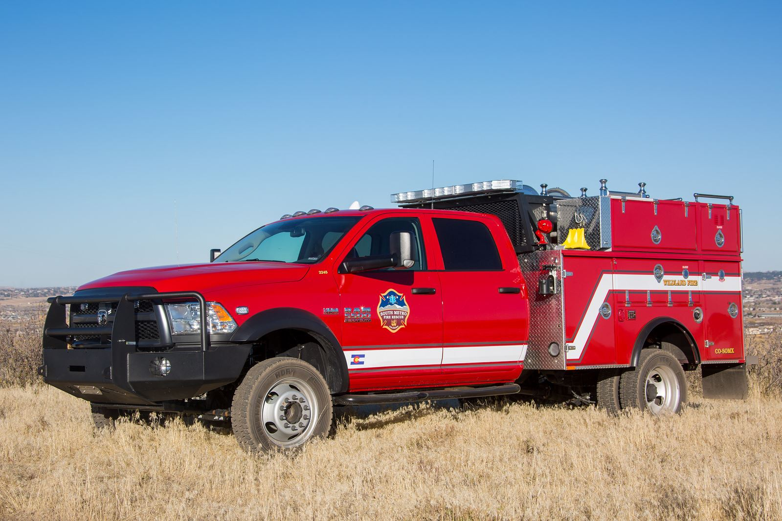 A red fire truck is parked on dry grassland under a clear blue sky.
