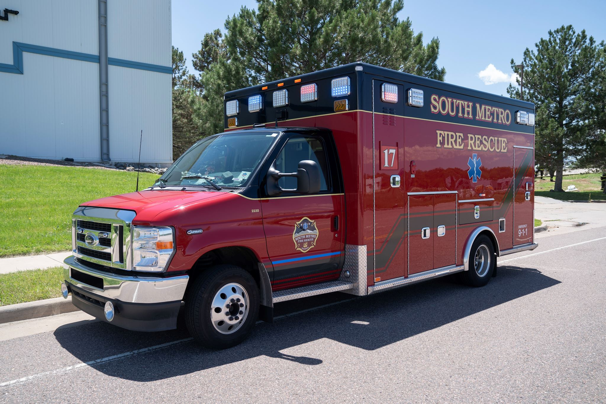 A red South Metro Fire Rescue ambulance parked near a building on a sunny day.