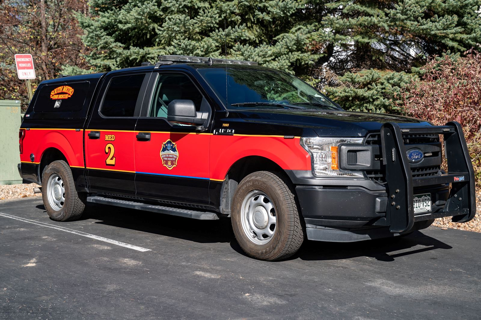 A red and black fire department rescue truck parked beside trees.