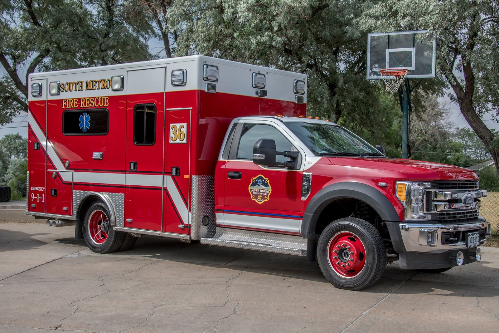 A red and white emergency vehicle for South Metro Fire Rescue parked outdoors near a basketball hoop.