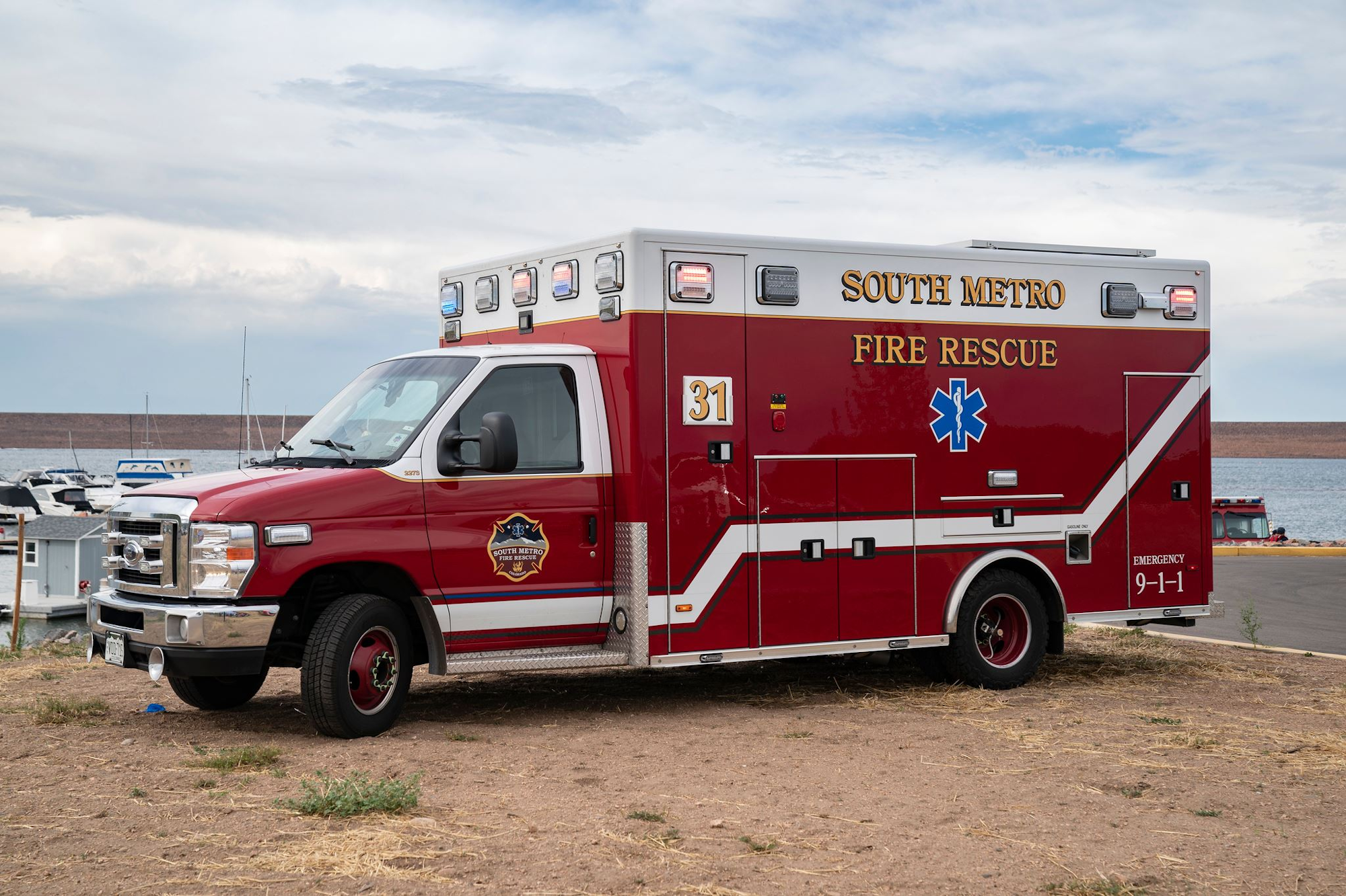 Red fire rescue ambulance parked near water and boats.