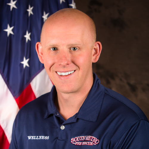 The image features a smiling individual in a navy shirt with "WELLNESS" and "SOUTHMETRO FIRE RESCUE," against an American flag backdrop.