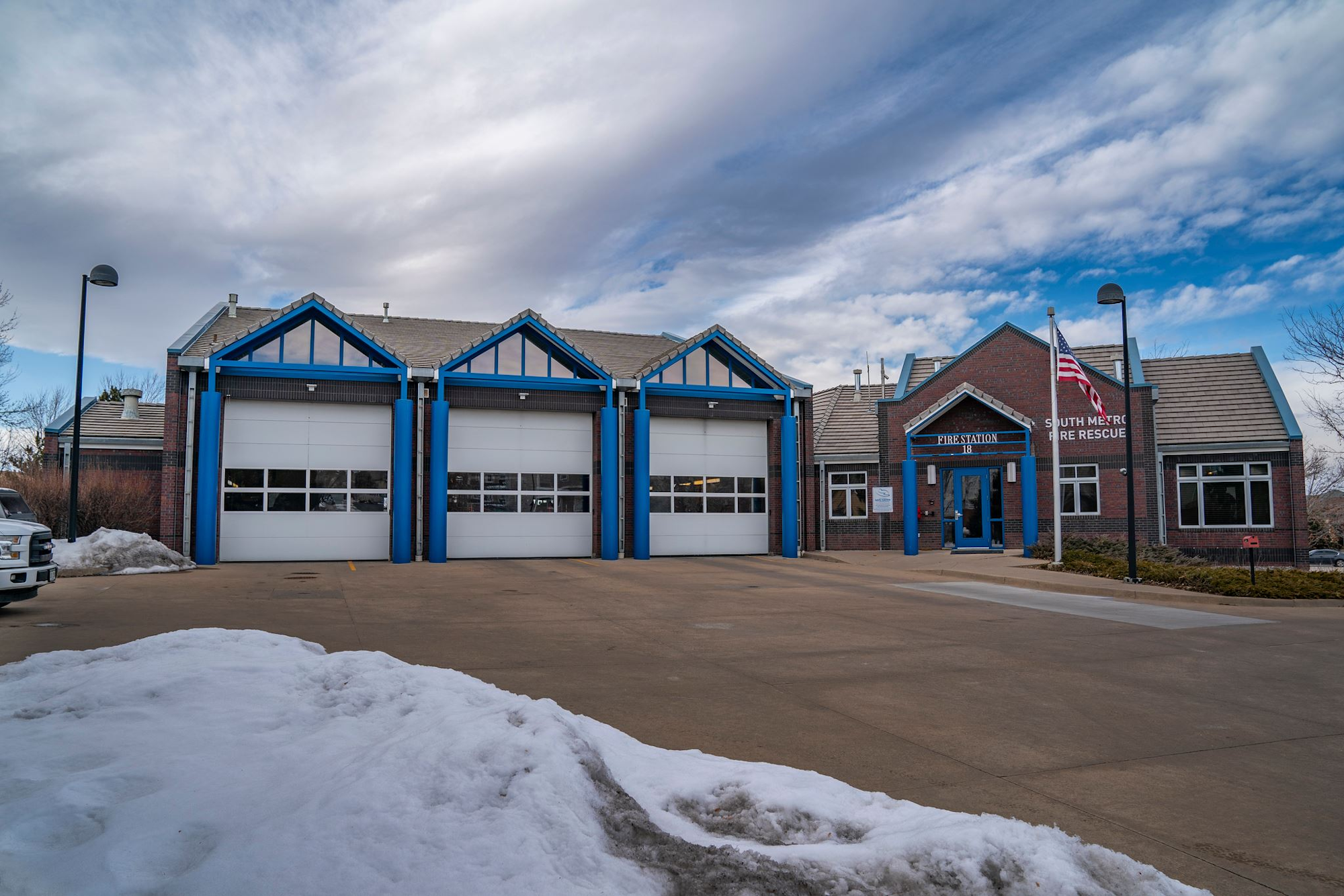 Fire station with three garage bays, American flag, and snow on the ground.