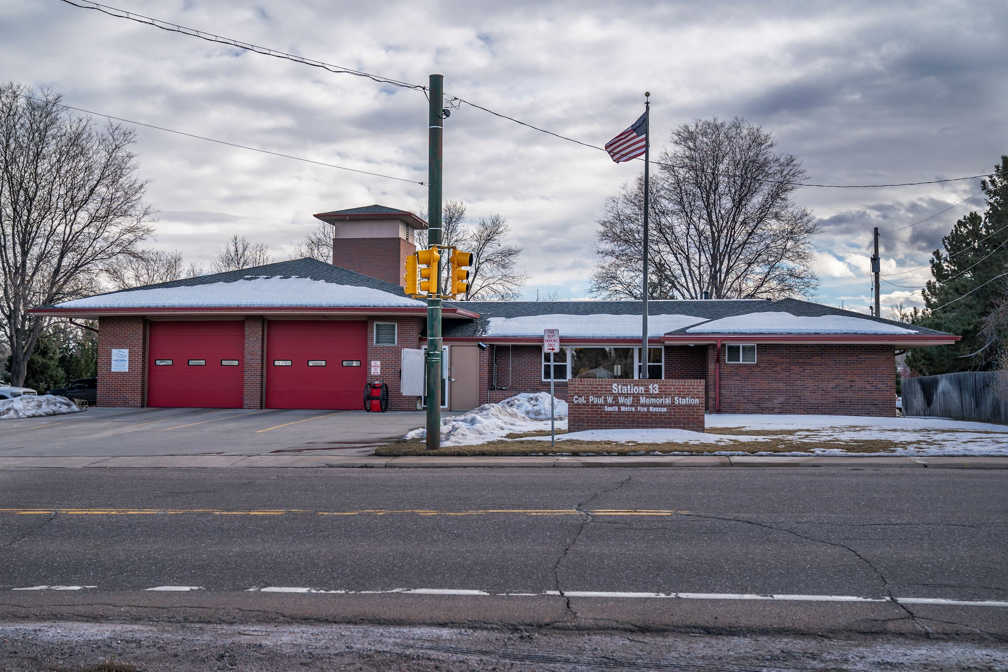 A fire station with red doors, an American flag, and a sign reading "Station 13 Col. Paul W. Wolf Memorial Station."