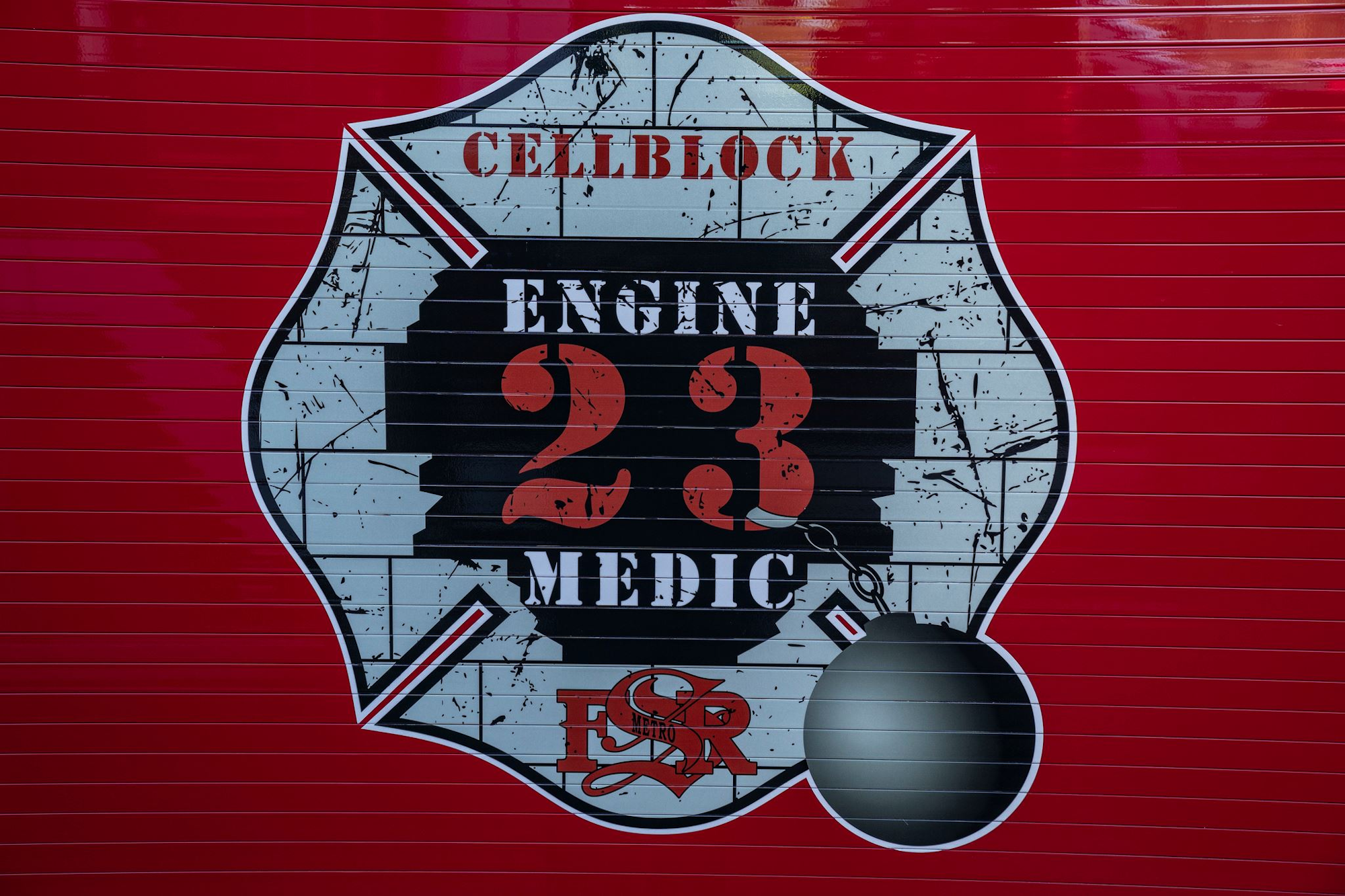 A red fire truck with a logo for "CELLBLOCK ENGINE 23 MEDIC" and an illustration of a wrecking ball.