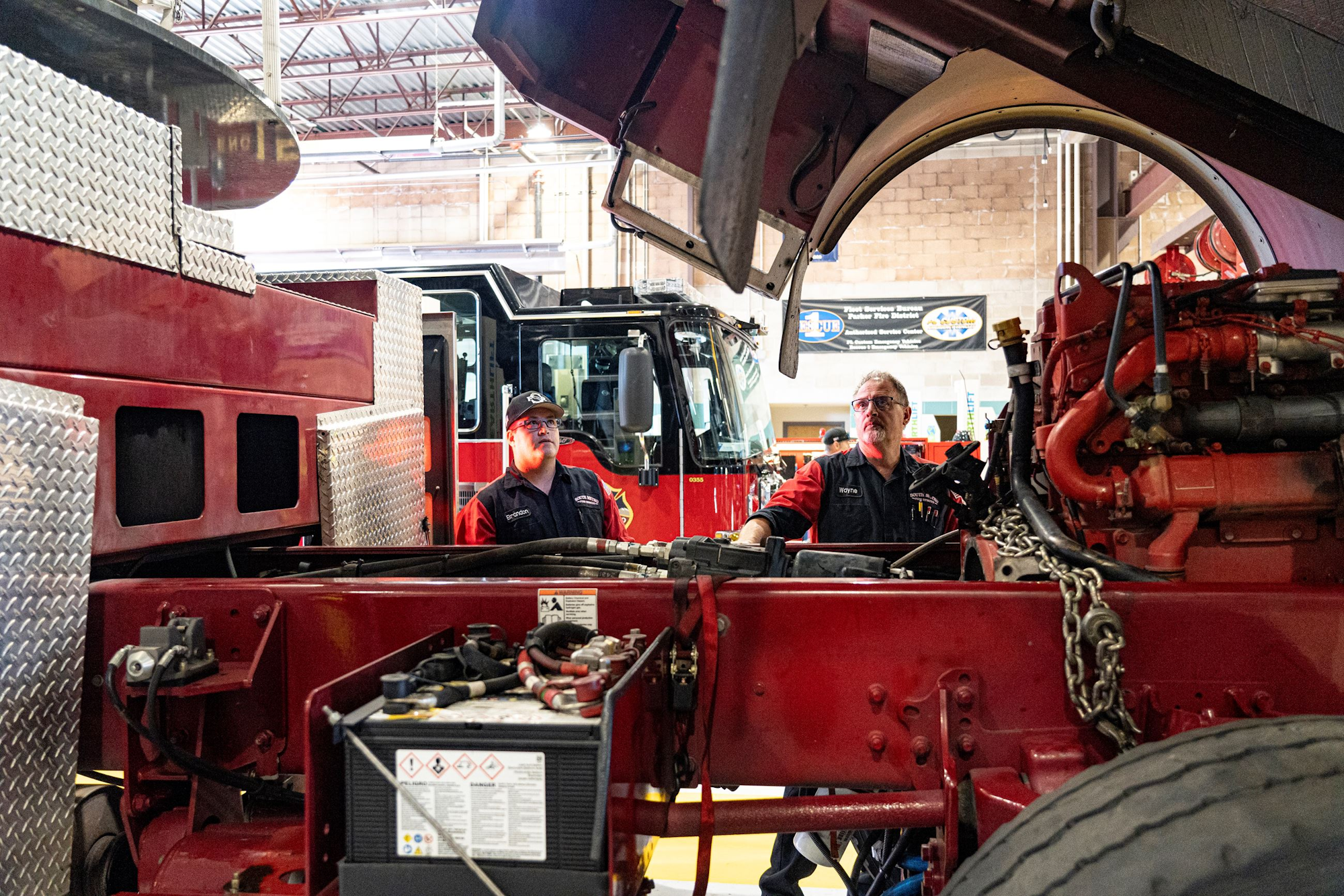 Two mechanics inspect a fire truck engine in a garage.