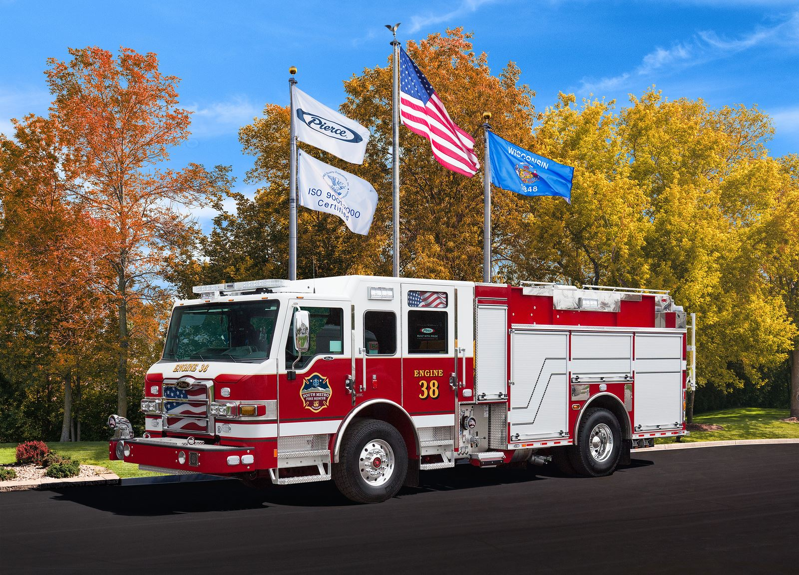 Red and white fire truck with "Engine 38," under three flags, against autumn trees and blue sky backdrop.