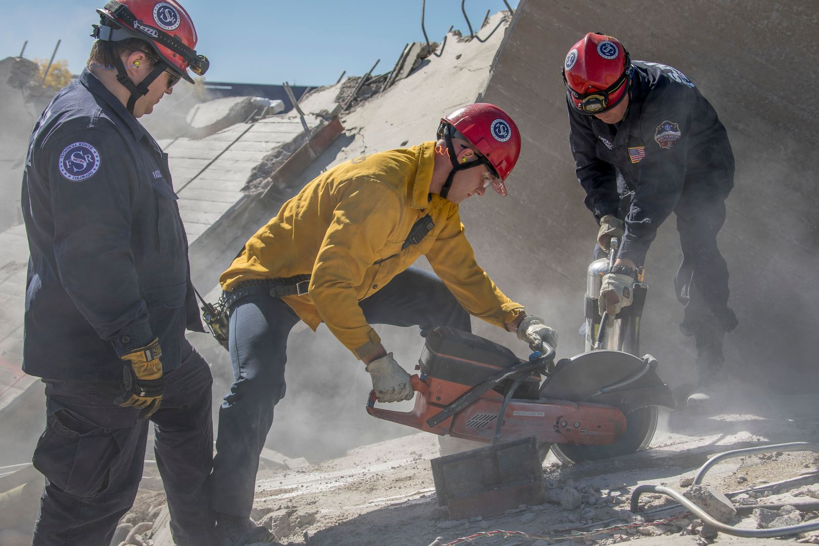 Rescue workers in helmets and uniforms using tools amidst rubble.