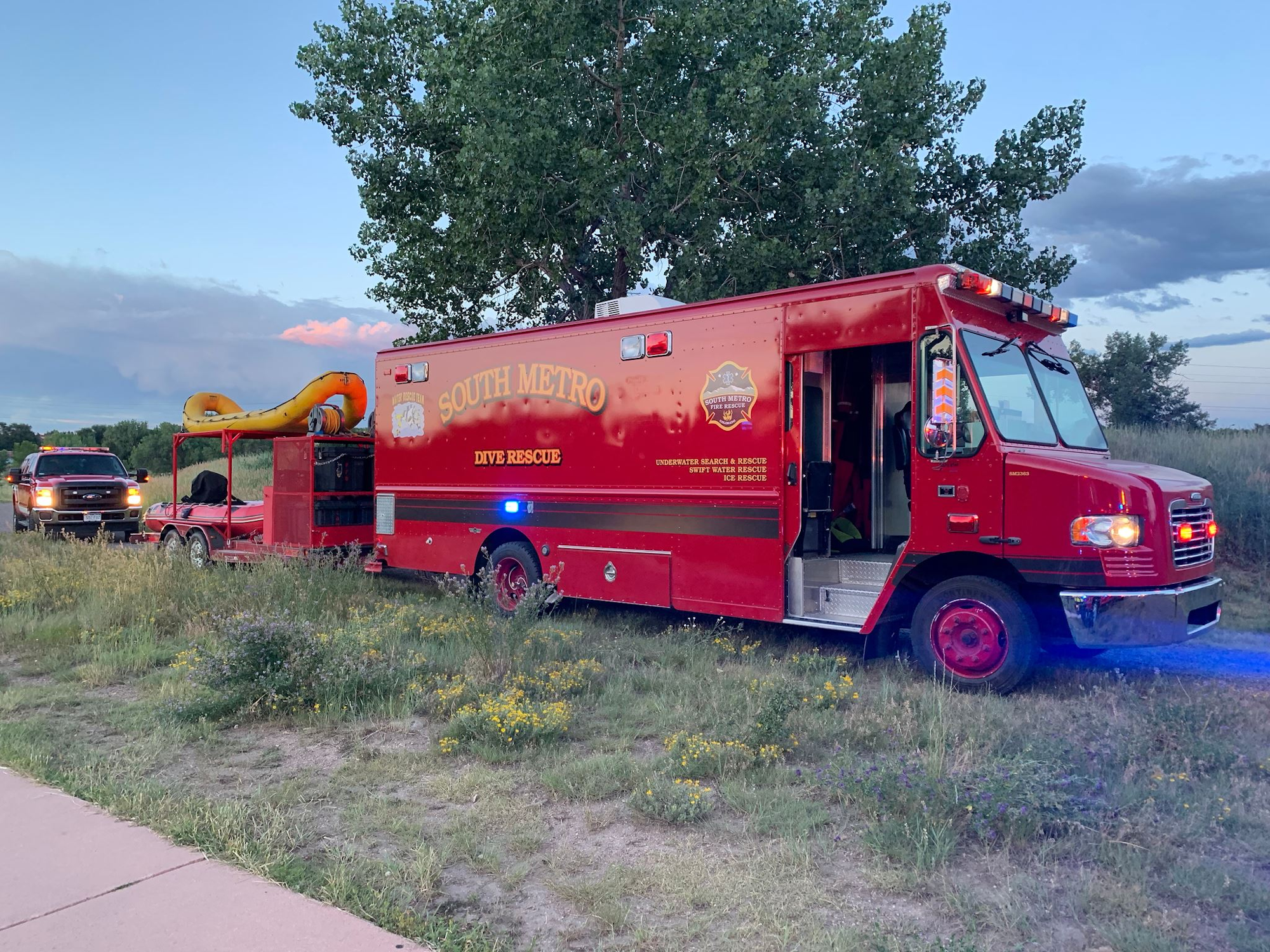 A South Metro Dive Rescue vehicle with a trailer and raft is parked on grass near a road.