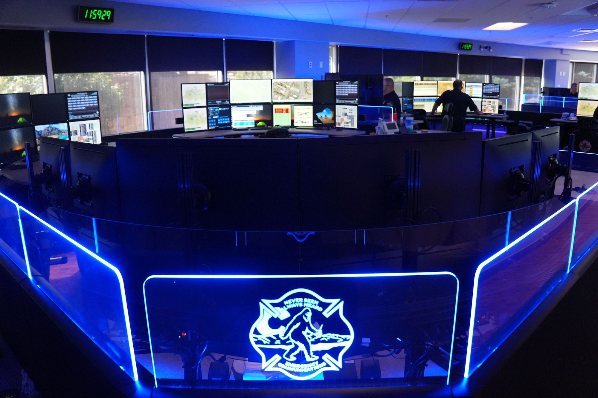 A control room with multiple monitors and a blue-lit counter, featuring a logo of Sasquatch and the phrase "Never Seen, Always Heard."