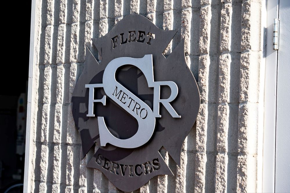 A "Fleet Services" metal sign on a brick wall with the letters "FSR" and "Metro" in the center.