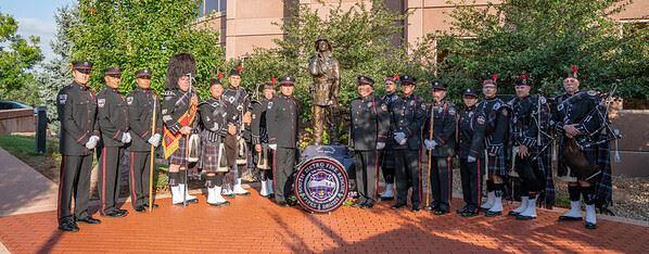 A group in uniform poses near a statue with bagpipes and a drum.