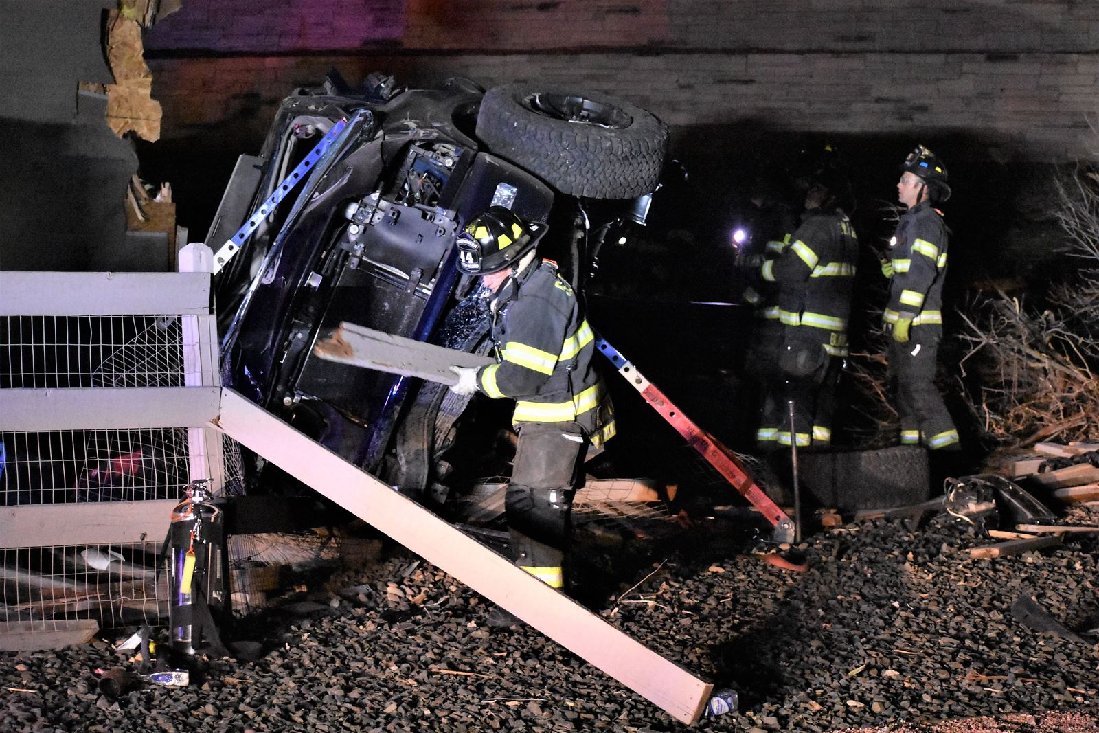 Firefighters respond to an overturned vehicle crash at night, debris scattered around.