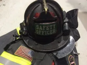 A firefighter's helmet labeled "Safety Officer" rests on a fire uniform, showcasing safety equipment and an American flag patch.