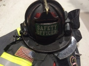 A firefighter's helmet labeled "Safety Officer" rests on a fire uniform, showcasing safety equipment and an American flag patch.