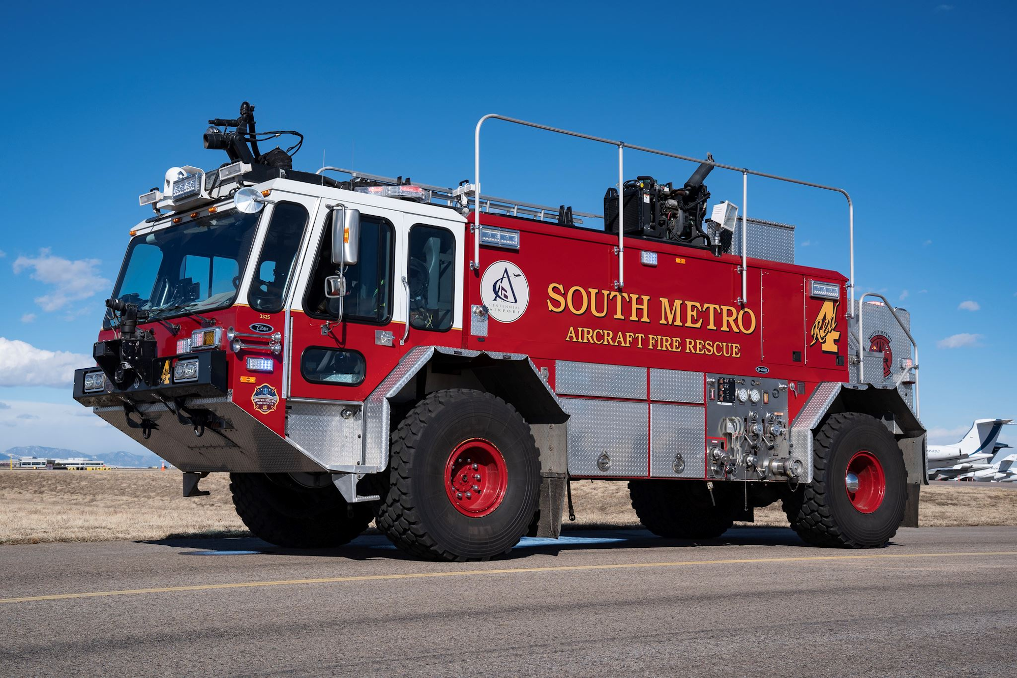 Red aircraft fire rescue truck on a tarmac under a clear blue sky.