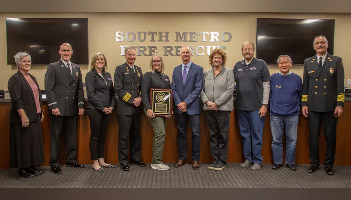 A group of people standing in front of a "South Metro Fire Rescue" sign, with one person holding a framed award.