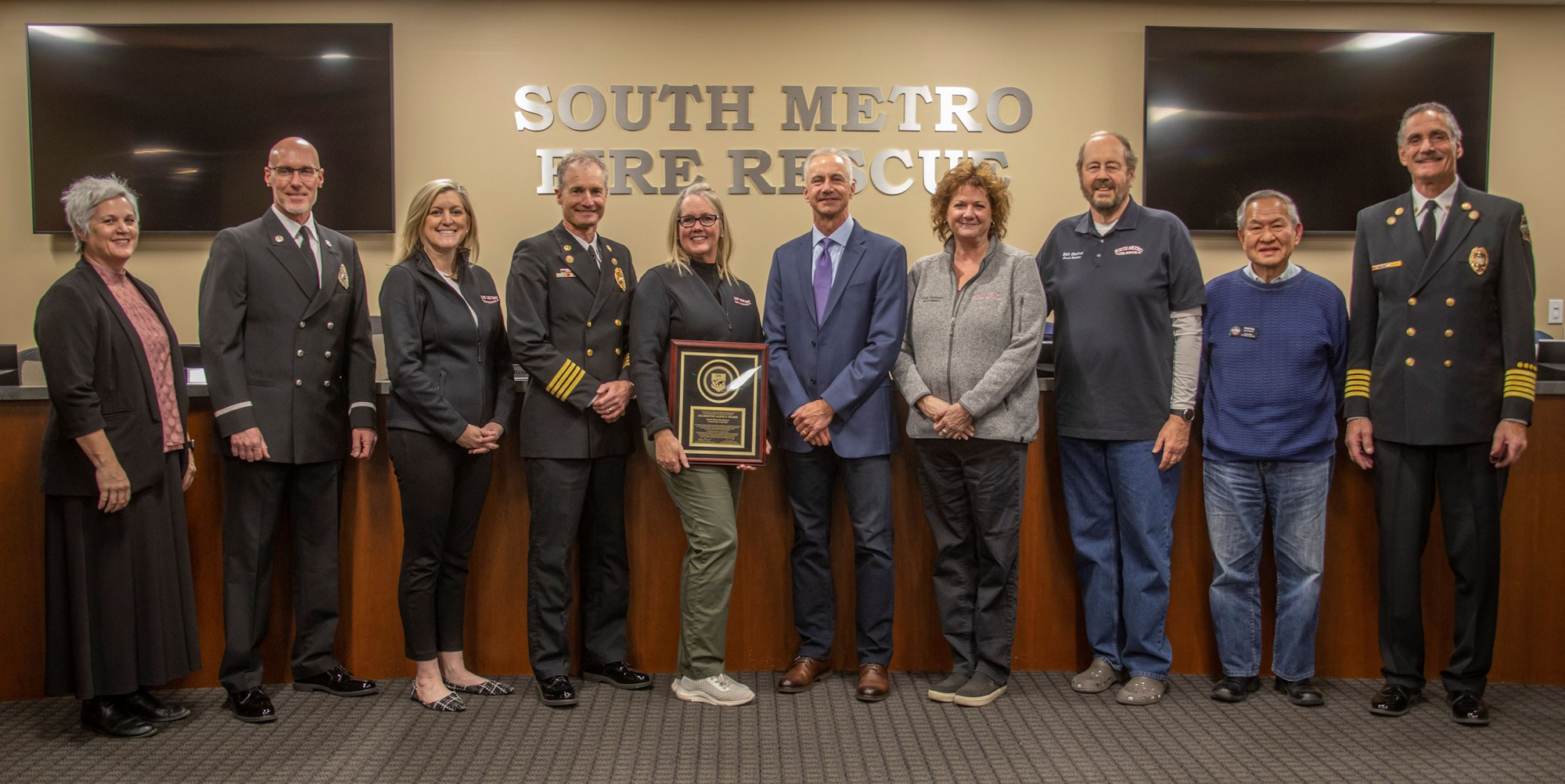 A group of people standing in front of a "South Metro Fire Rescue" sign, with one person holding a framed award.