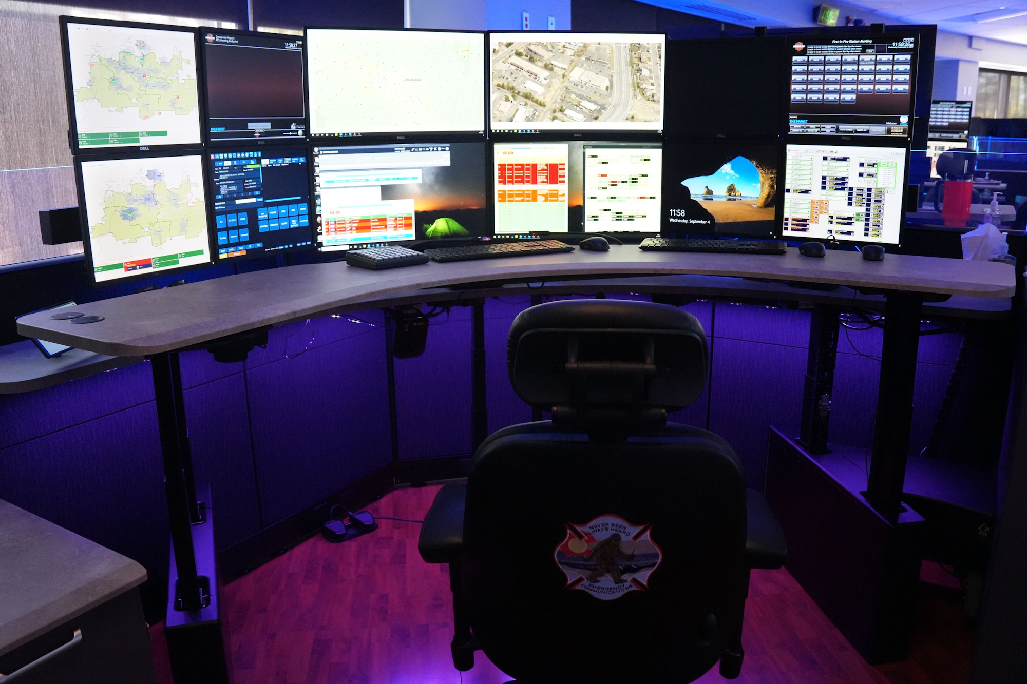 A command center with multiple computer monitors, a chair, and lit with purple LED lighting.