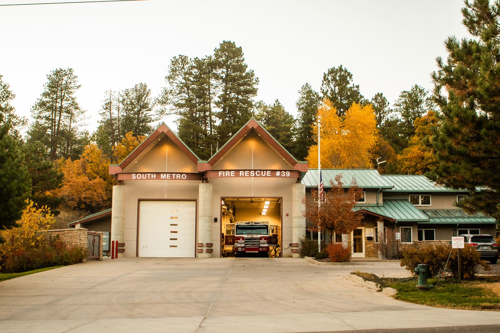 Fire station with a fire truck in the garage, surrounded by trees with autumn foliage.