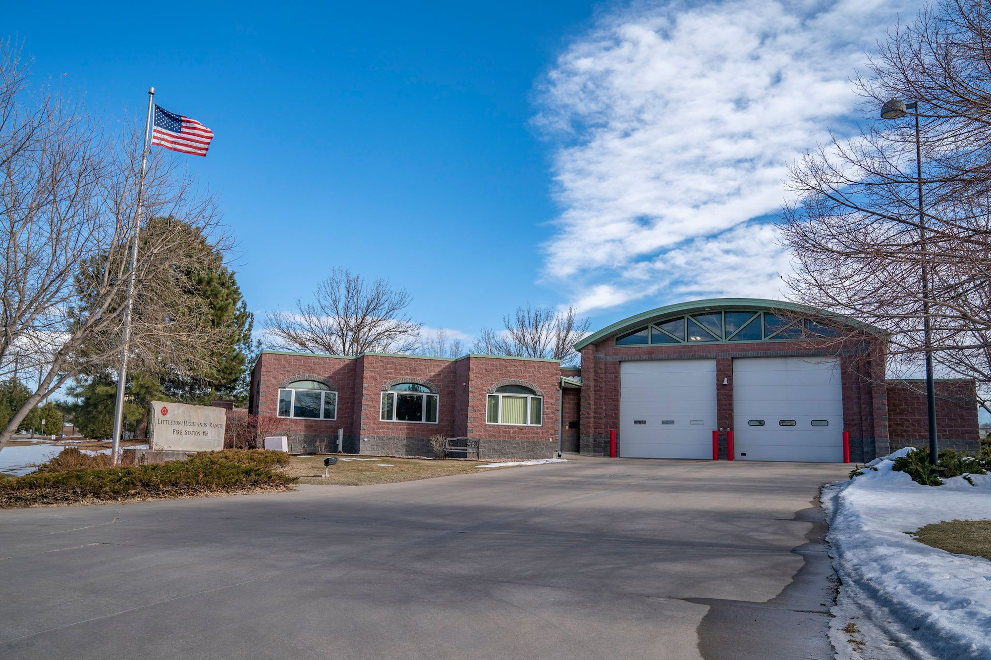 Fire station with two garage bays, an American flag, trees, and clear blue skies.