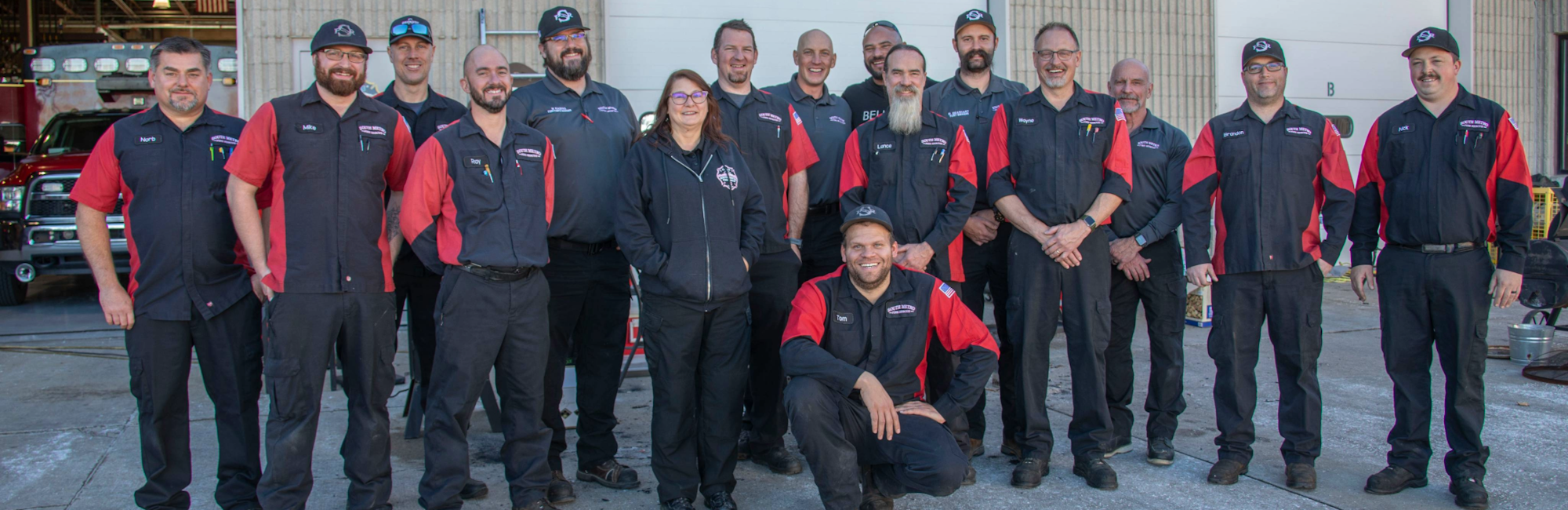 A group of people wearing matching uniforms, standing and posing in front of a garage with vehicles inside.