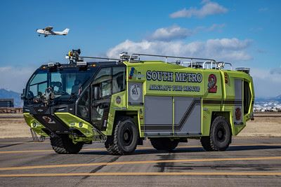 A green airport fire truck labeled "South Metro Aircraft Fire Rescue" is on a runway, with a small plane flying above.
