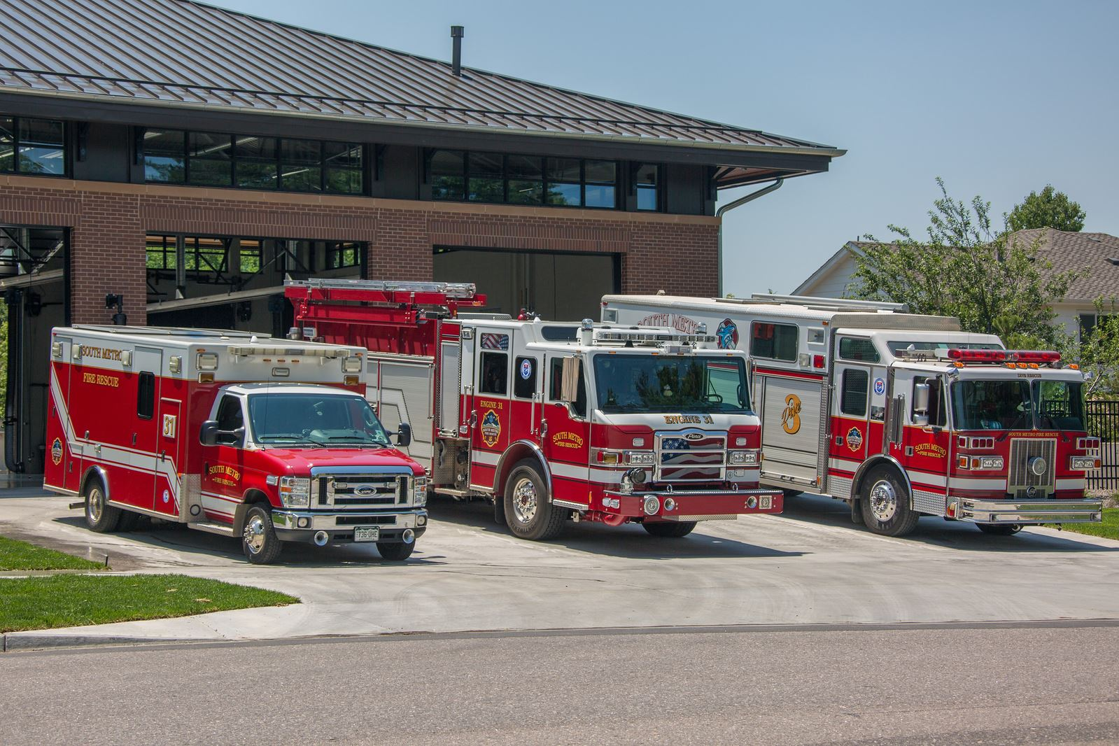 Three red fire trucks parked in front of a fire station.