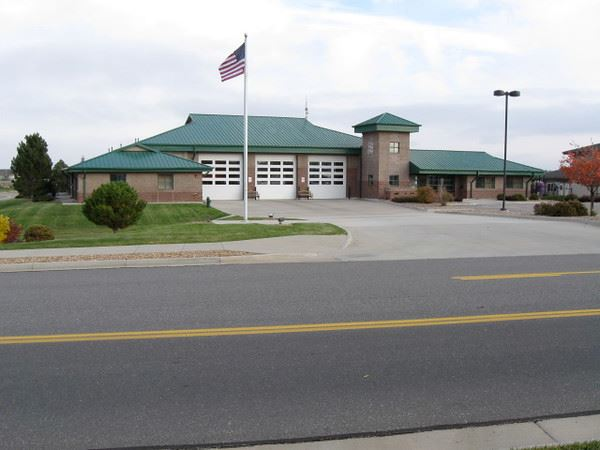 A fire station with a green roof, American flag, garage doors, and a paved driveway.