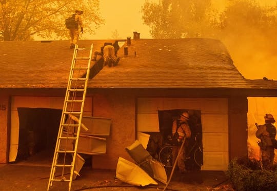 Firefighters on and around a house under an orange smoky sky.