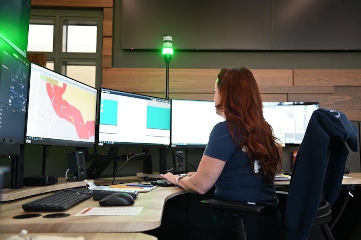 Person at a desk with multiple computer monitors showing maps and data.