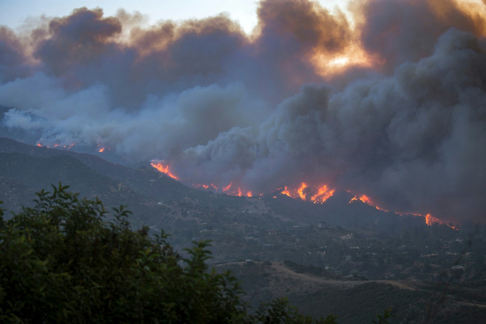 A large wildfire consumes a hillside, with thick smoke and visible flames.