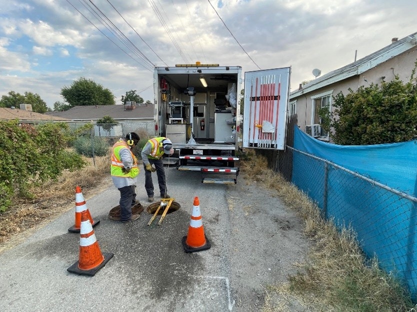 Two workers in safety vests with traffic cones and a utility truck working in an alley.