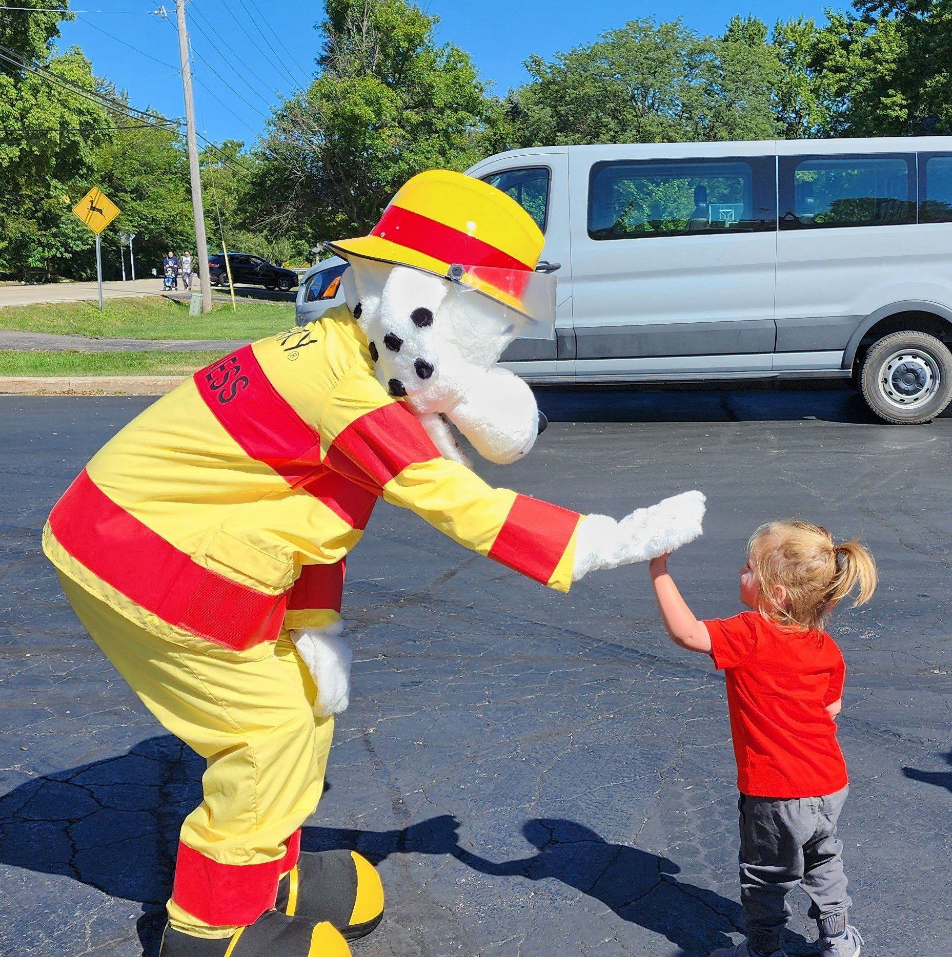 A person in a Dalmatian fireman costume high-fives a young child in red outdoors.