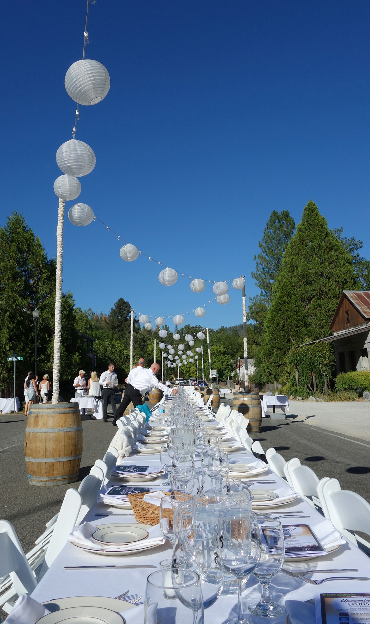 Dining setup on Main St. Volcano with a long table, white paper lanterns, and guests mingling under a clear blue sky.