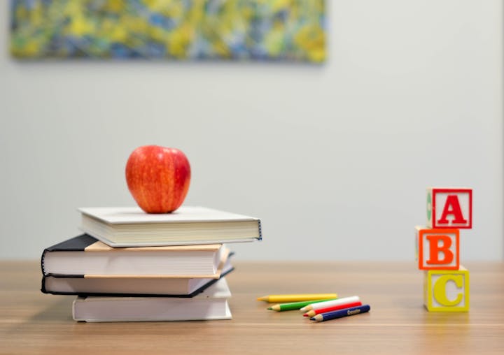 A stack of books with an apple on top, colored pencils, and ABC blocks on a table.