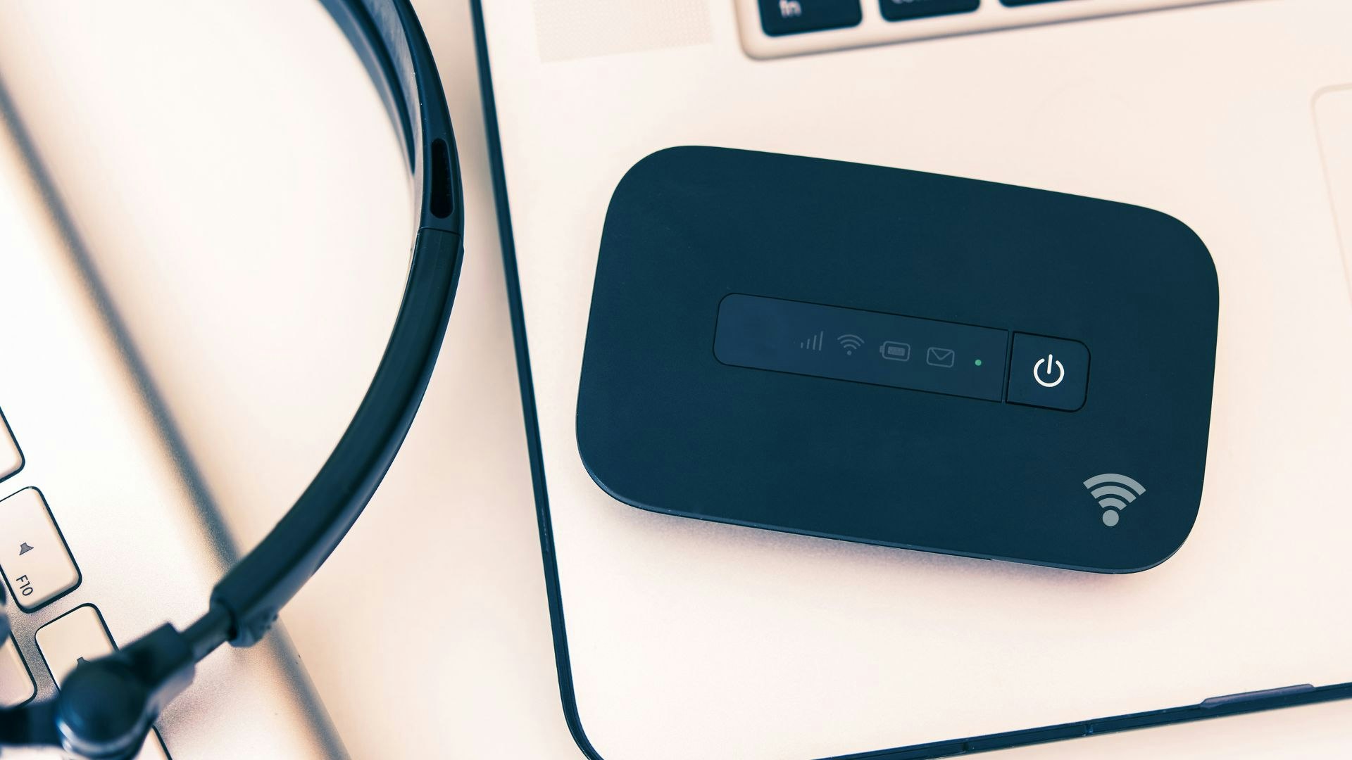 A headset and a portable Wi-Fi router on a laptop keyboard.