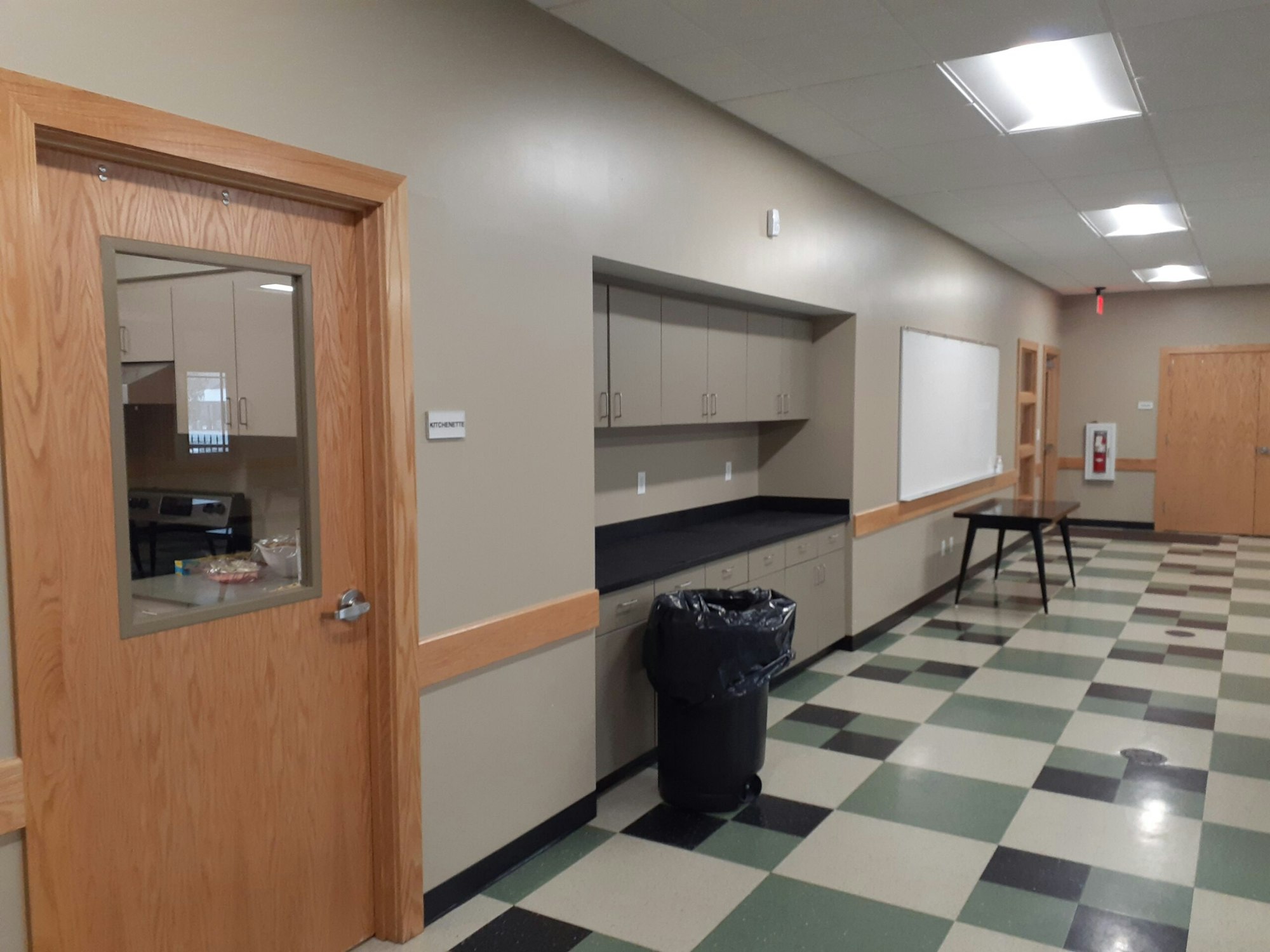 A hallway with tiled floor, cabinets, a trash bin, and a door labeled "Kitchenette."