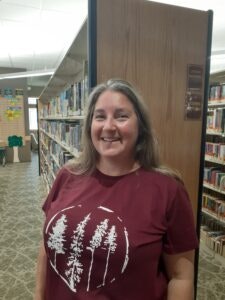 A person in a library wearing a maroon shirt with tree design.