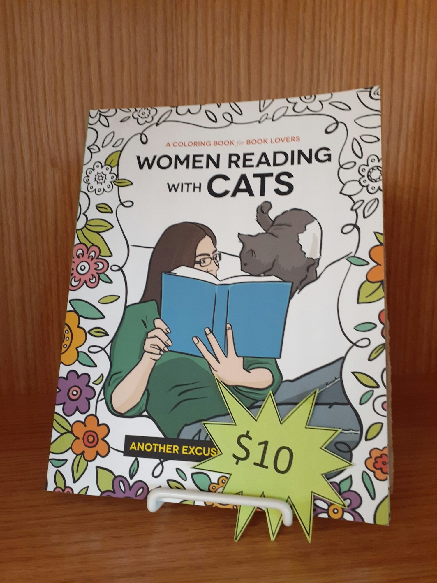 A coloring book titled "Women Reading with Cats," priced at $10, featuring flowers and a woman with a cat.