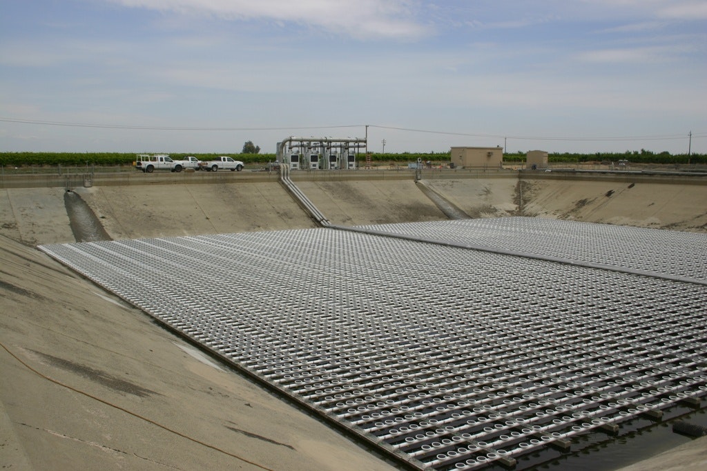 The image shows a large water treatment facility with a grid system, pipes, and vehicles, set in a rural landscape.