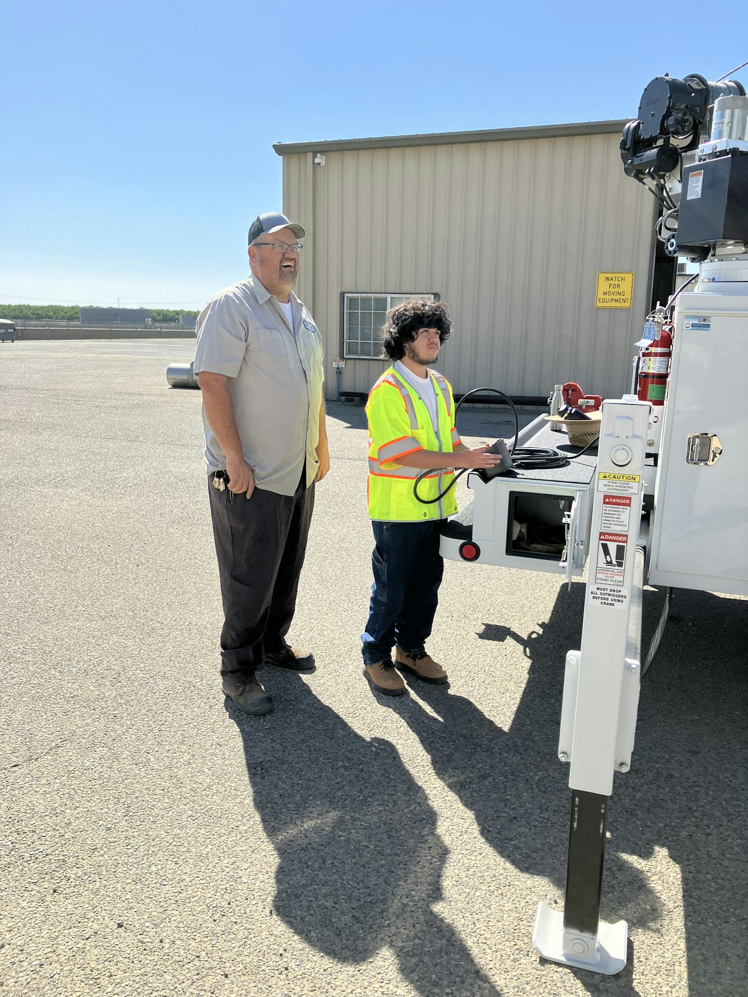 Two people in safety vests stand near a utility vehicle on a sunny day.