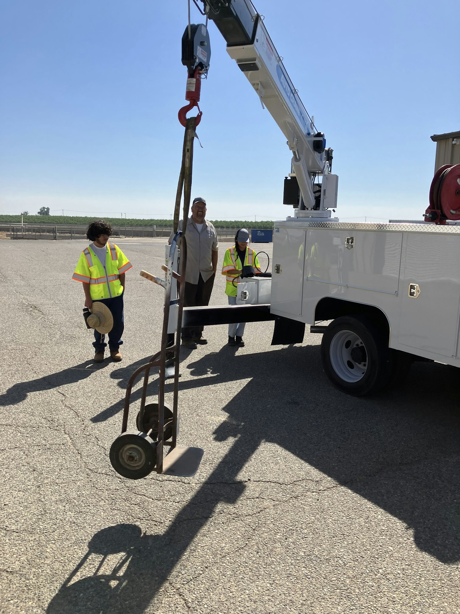 A crane lifting an object, with two workers in safety vests standing nearby on a paved surface.
