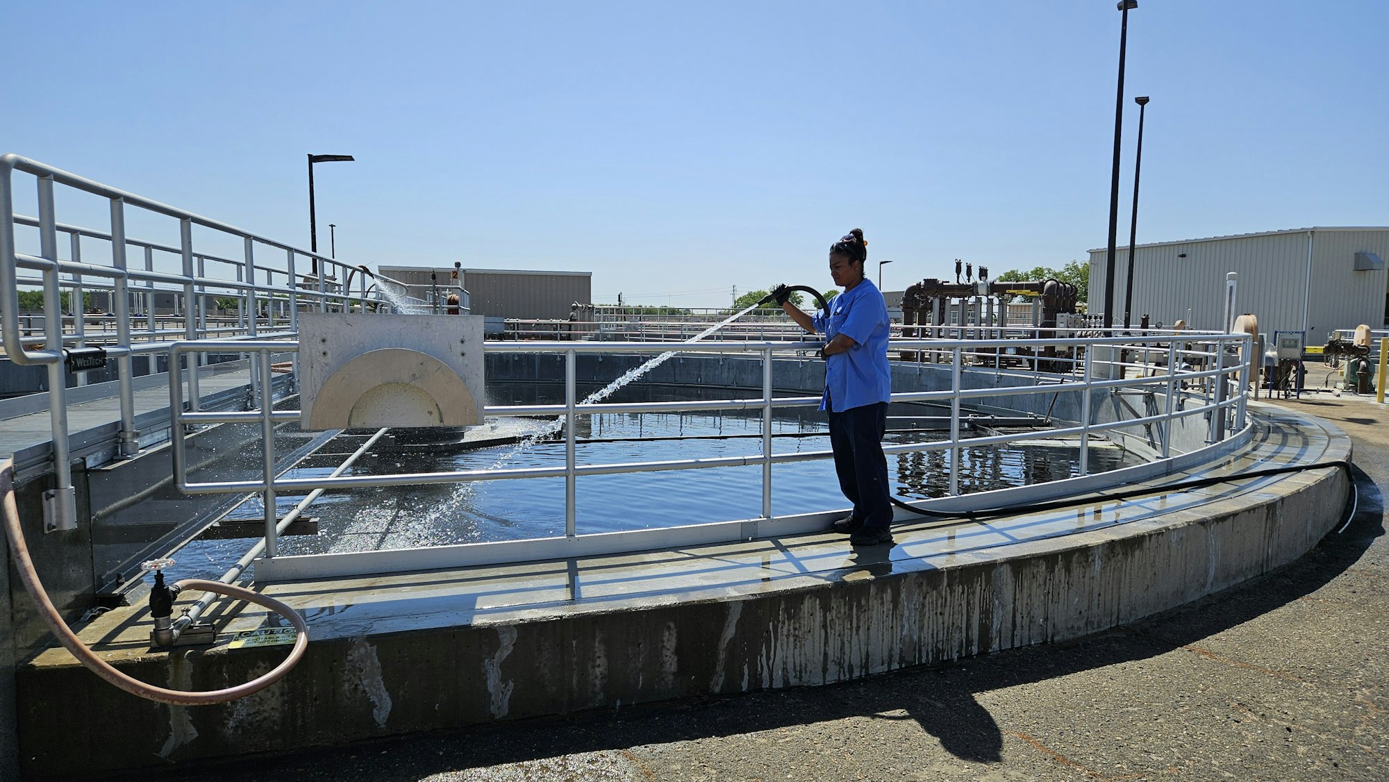 A worker sprays water into a treatment tank at a facility on a sunny day.