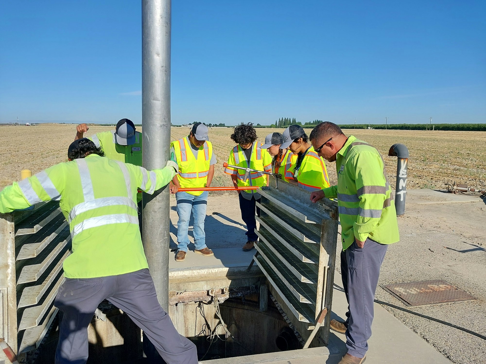 A group of workers in high-visibility vests inspect an open utility area outdoors.